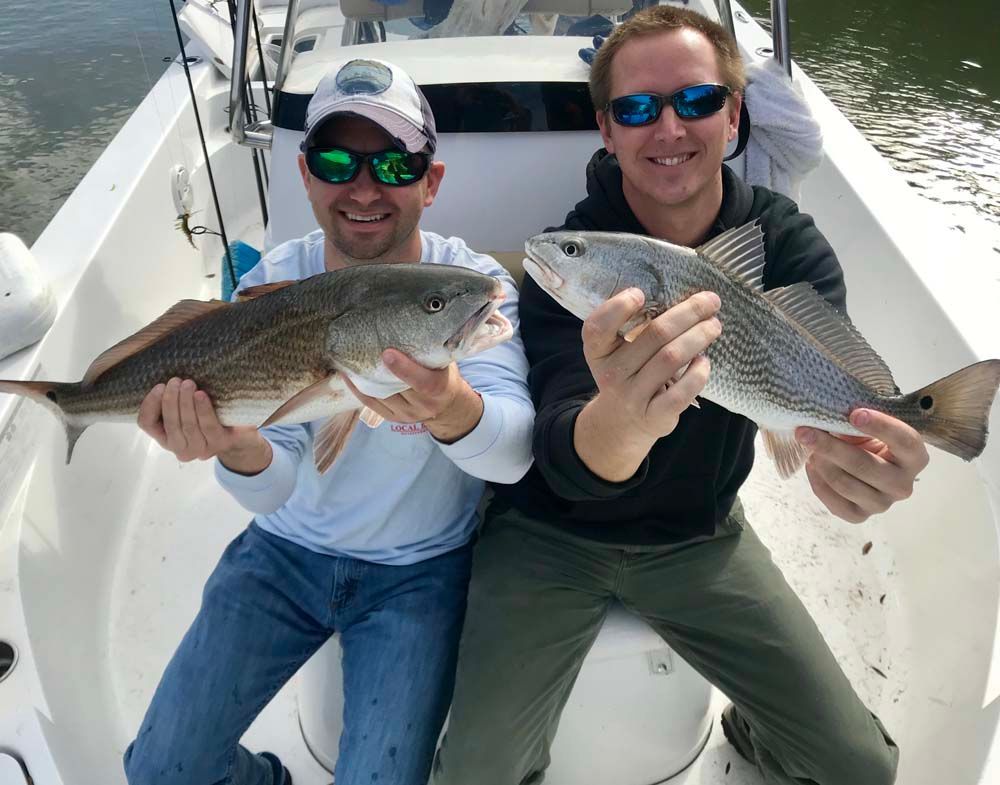 Two men on a boat holding large fish and smiling at the camera