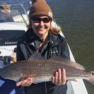Smiling person on a boat holding a large fish by the water
