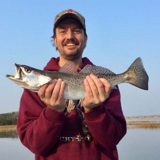 Man smiling and holding a large fish outdoors by the water at sunset