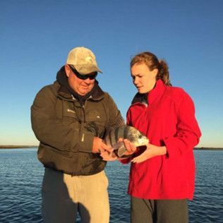 Two people holding a fish by calm water under a clear blue sky
