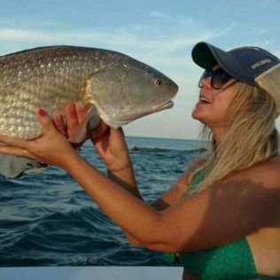 Woman holding a large fish above the water at sea, wearing a cap and sunglasses.
