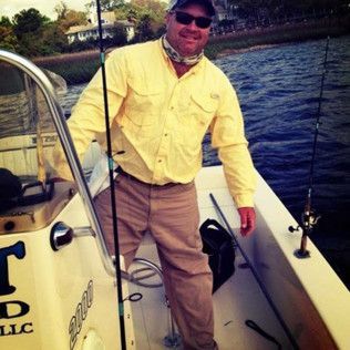 Man in yellow shirt and cap standing on a boat holding a fishing rod on the water