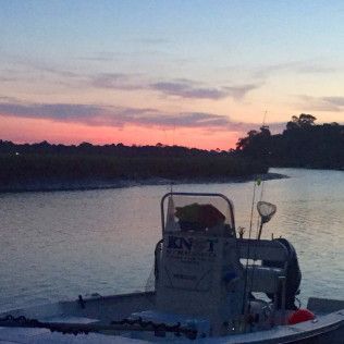 Small boat on calm water at sunset, with a pink-orange sky and dark shoreline silhouettes