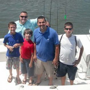 Five people standing on a boat deck with water in the background, smiling at the camera.
