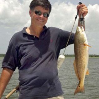 Man holding up a large fish while smiling on a boat, wearing sunglasses and a dark polo shirt.