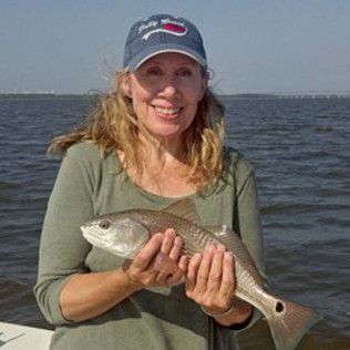 Woman smiling while holding a fish on a boat with water in the background