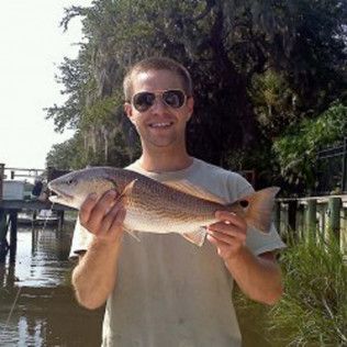 Man smiling while holding a large fish beside a canal on a sunny day