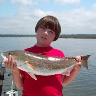 Person in a red shirt holding a large fish by the water