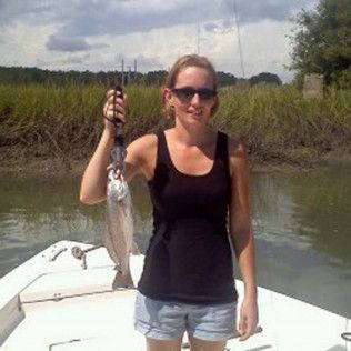 Woman on a boat holding up a fish in a marshy waterway.