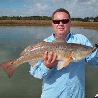 Man in sunglasses holding a large fish by a calm lakeshore
