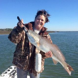 Person holding a large fish on a boat in calm blue water under a clear sky