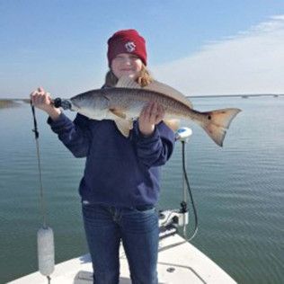 Person on a boat holding a large fish over calm water, wearing a red beanie and navy sweatshirt.