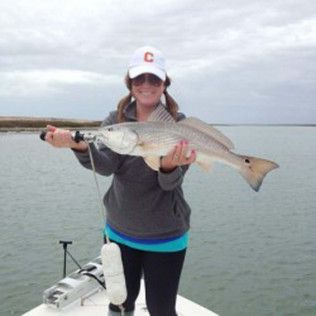 Person on a boat holding a large fish, smiling, with calm water in the background.