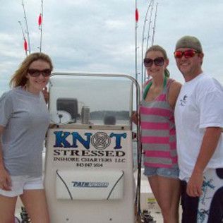 Three people standing on a boat next to a “KNOT STRESSED” sign.