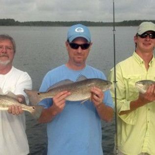 Three anglers holding fish on a boat with a calm lake in the background