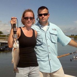 Two people on a boat holding a fish, both wearing sunglasses under a clear sky
