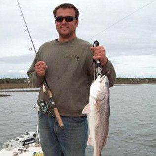 Man holding two fishing rods and a large fish on a boat on calm water