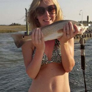 Woman in sunglasses holding a large fish by the water at sunset