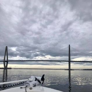 Boat on calm water near a cable-stayed bridge under a cloudy sky