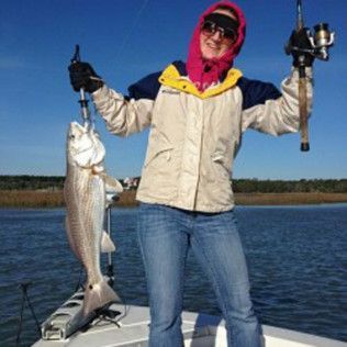 Angler on a boat holding a large fish and fishing rod, with a lake and blue sky in the background.