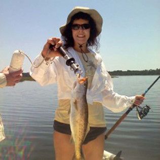 Person holding a large fish on a boat, smiling by calm water while fishing