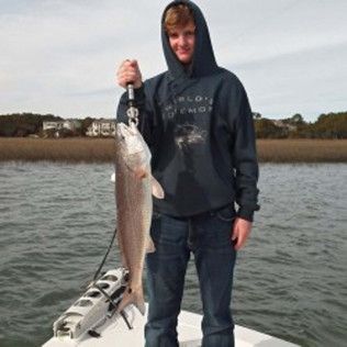 Person on a boat holding up a large fish over the water on an overcast day