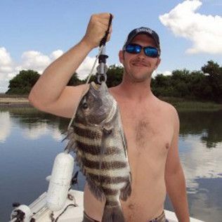 Man holding a large striped fish on a boat in a calm river