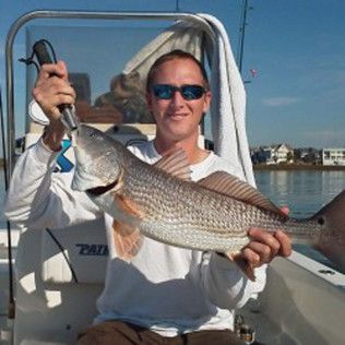Man on a boat holding a large silver fish, wearing sunglasses on a sunny day.