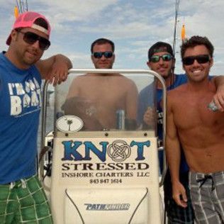 Four men posing on a boat behind a charter sign, two wearing sunglasses and one shirtless.
