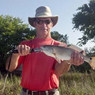 Man in a hat holding a large fish outdoors in tall grass under a bright sky