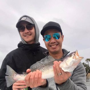 Two smiling anglers holding a large fish outdoors under an overcast sky
