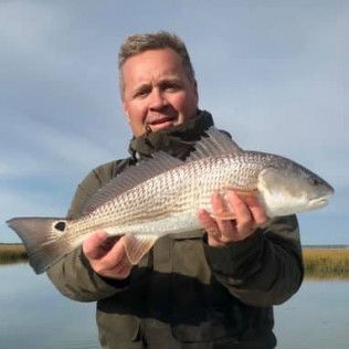 Man holding a large silver fish outdoors by calm water under a clear sky