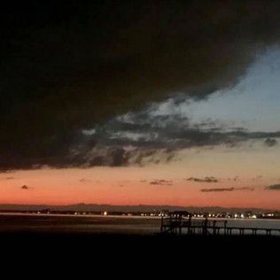 Dramatic sunset over a waterfront with dark clouds and distant city lights