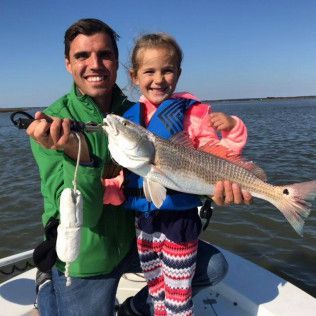 Adult and child on a boat holding up two fish on a sunny day