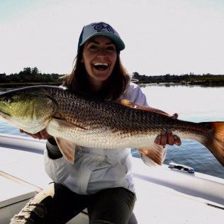 Person smiling and holding a large fish on a boat on calm water