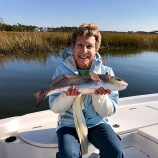 Person holding a large fish while sitting on a boat in a marsh