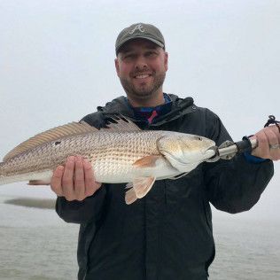 Smiling angler holding a large redfish on a foggy shoreline