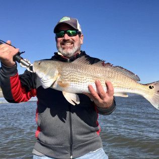Smiling angler holding a large fish on a boat with open water and blue sky behind him