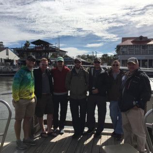 Group of six people standing together on a sunny dock by the water