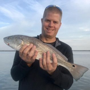 Man holding a large silver fish by the water at sunset