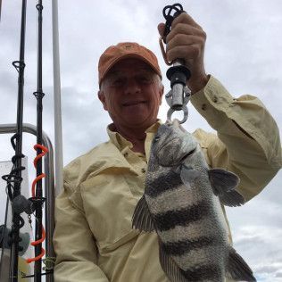 Angler holding a striped fish beside fishing rods on a cloudy day