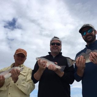 Three smiling people holding fish outdoors under a cloudy sky