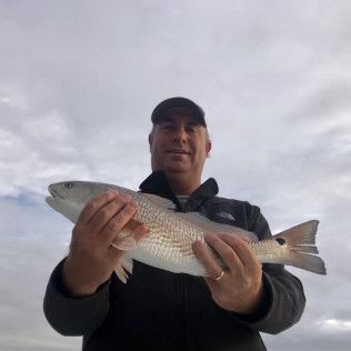 Person holding a silver fish outdoors under a cloudy sky