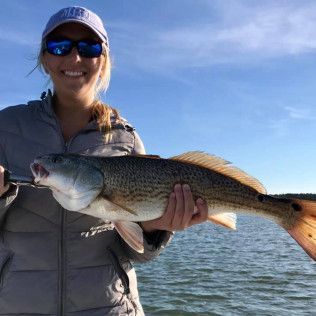 Smiling angler holding a large fish on a boat with blue water and sky in the background