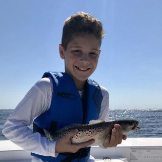 Boy holding a fish on a boat with the ocean in the background