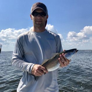 Man in sunglasses holding a fish on a boat under a blue sky