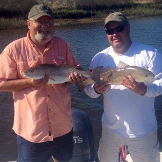 Two anglers on a boat holding large fish on a sunny river.