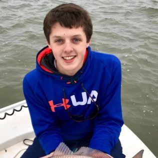 Smiling person in a blue hoodie sitting on a boat over gray water