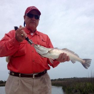 Man in red jacket and cap holding a large fish outdoors under a cloudy sky