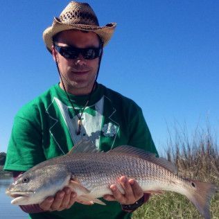 Man holding a large fish outdoors under a clear blue sky, wearing a straw hat and sunglasses